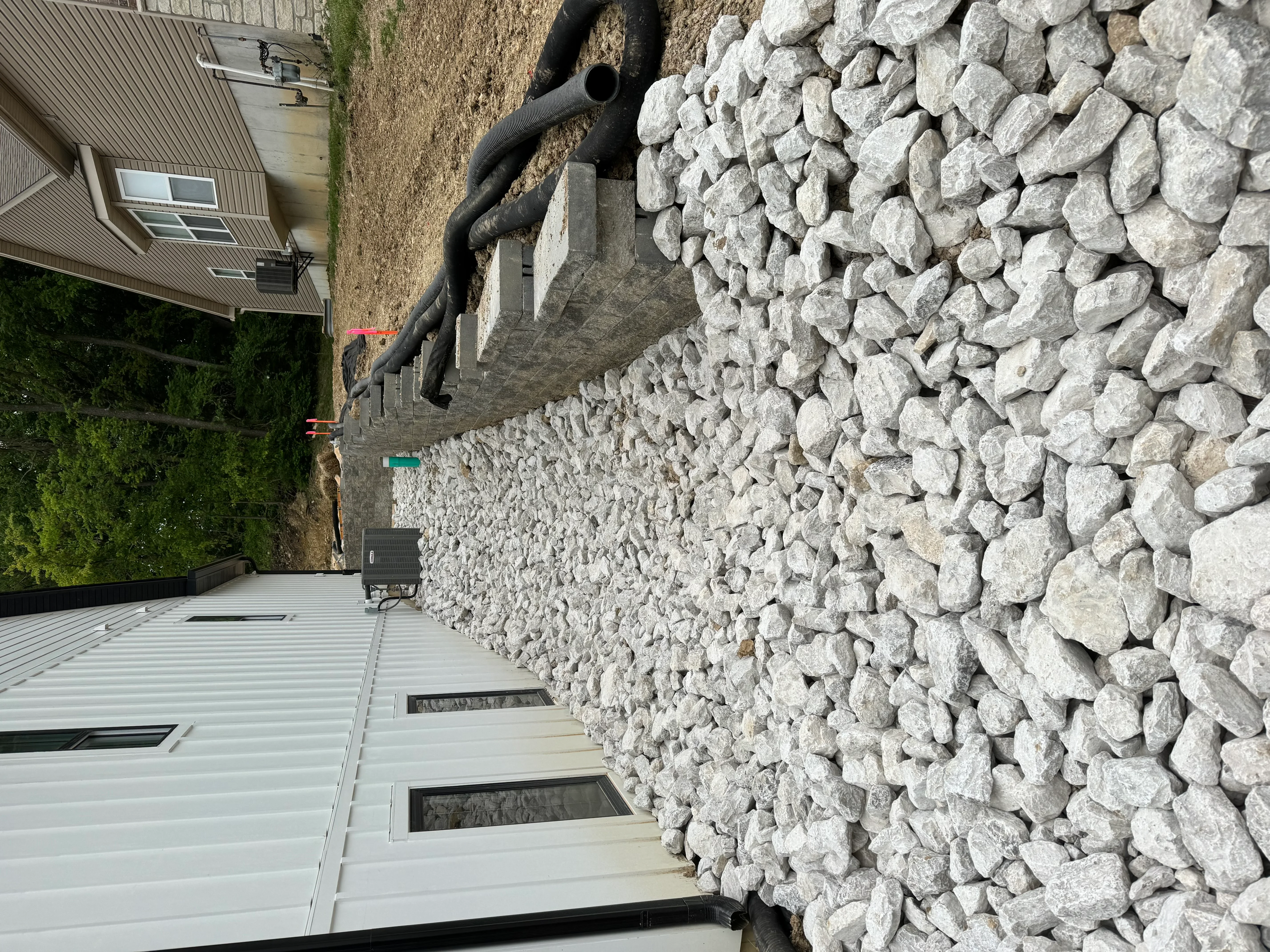 Gray stone retaining wall with drainage pipe and concrete foundation on residential property