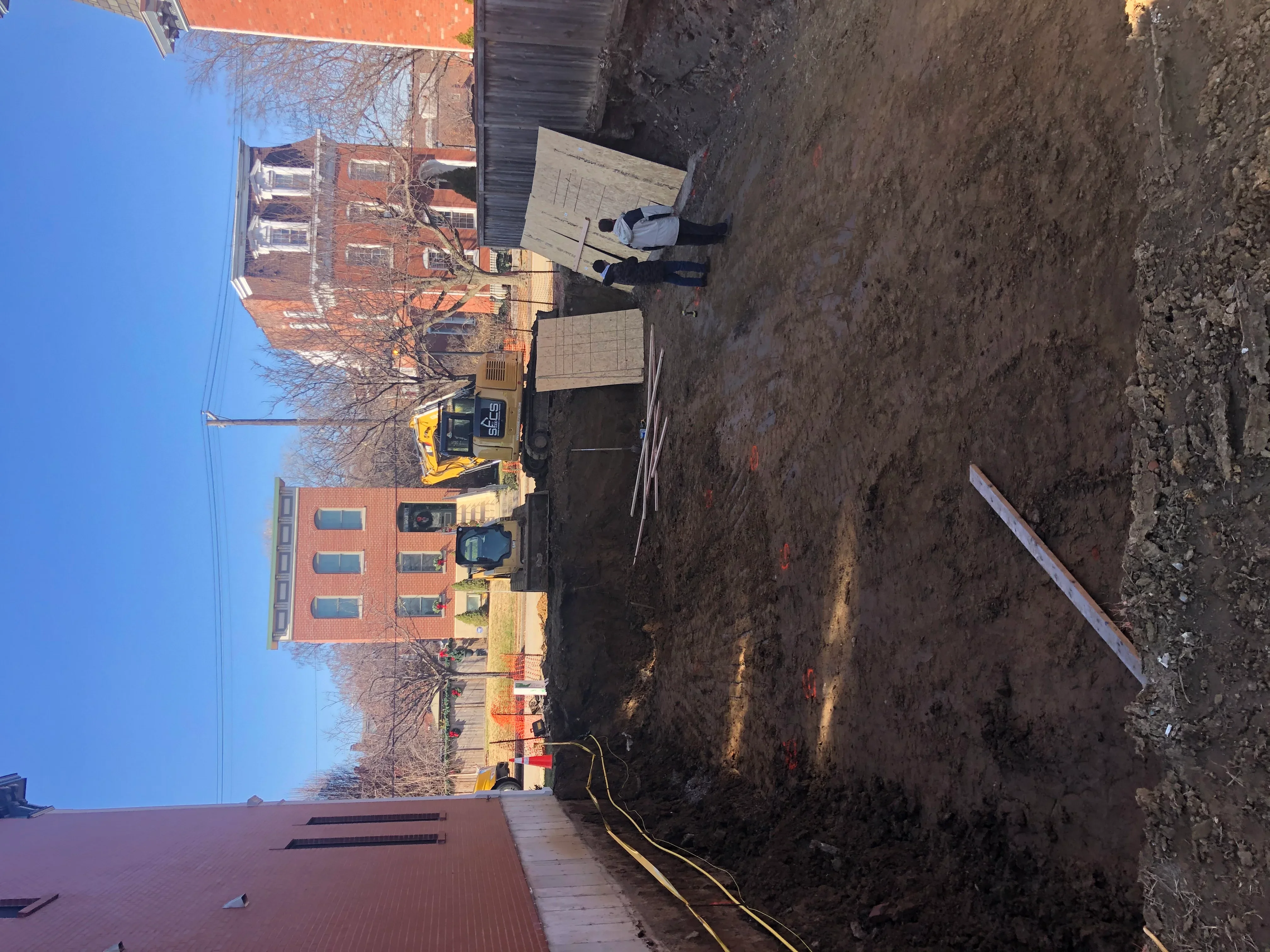 Excavator demolishing brick commercial building with debris removal on active job site