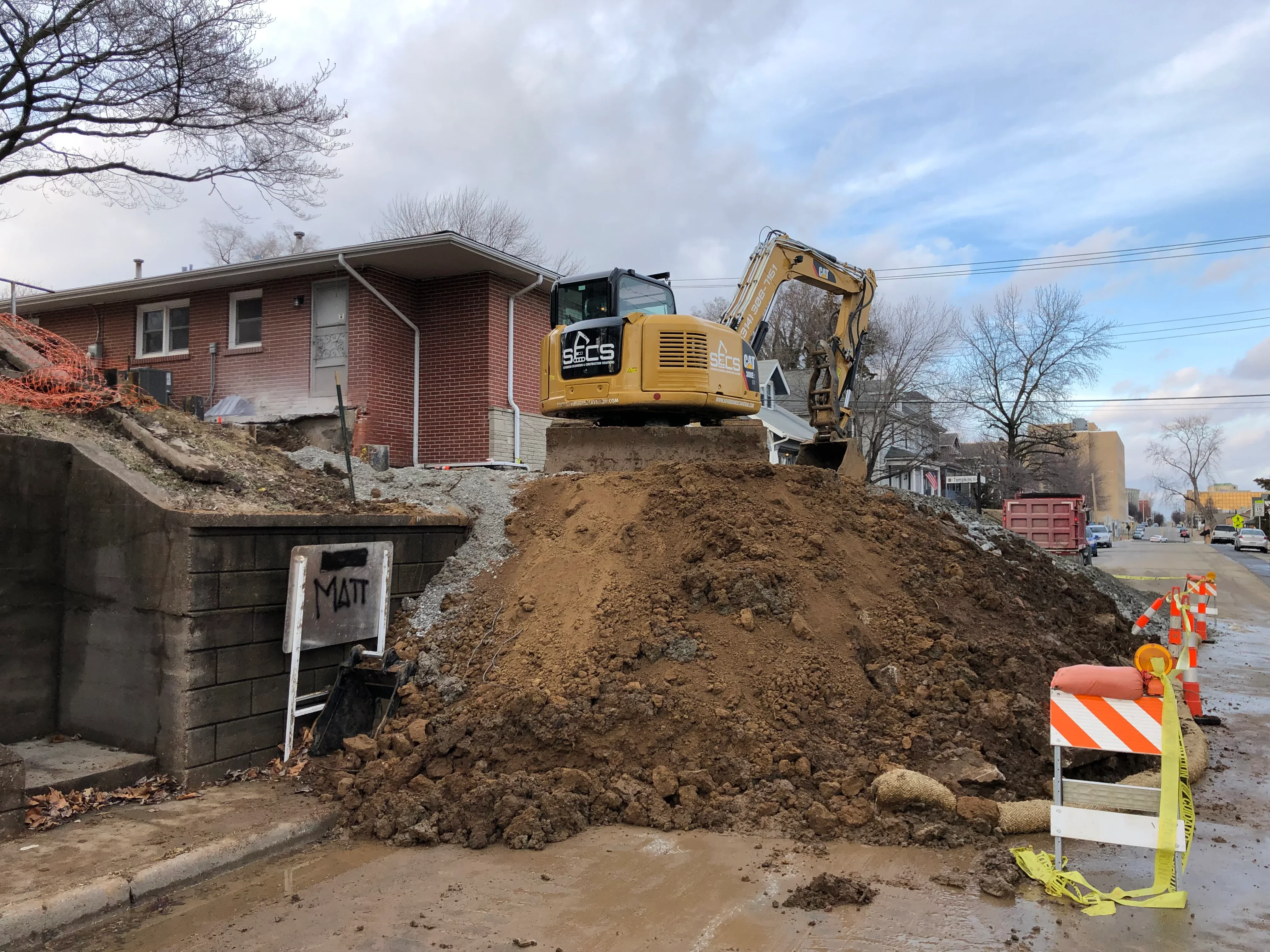 Yellow excavator on large dirt pile during residential site excavation work