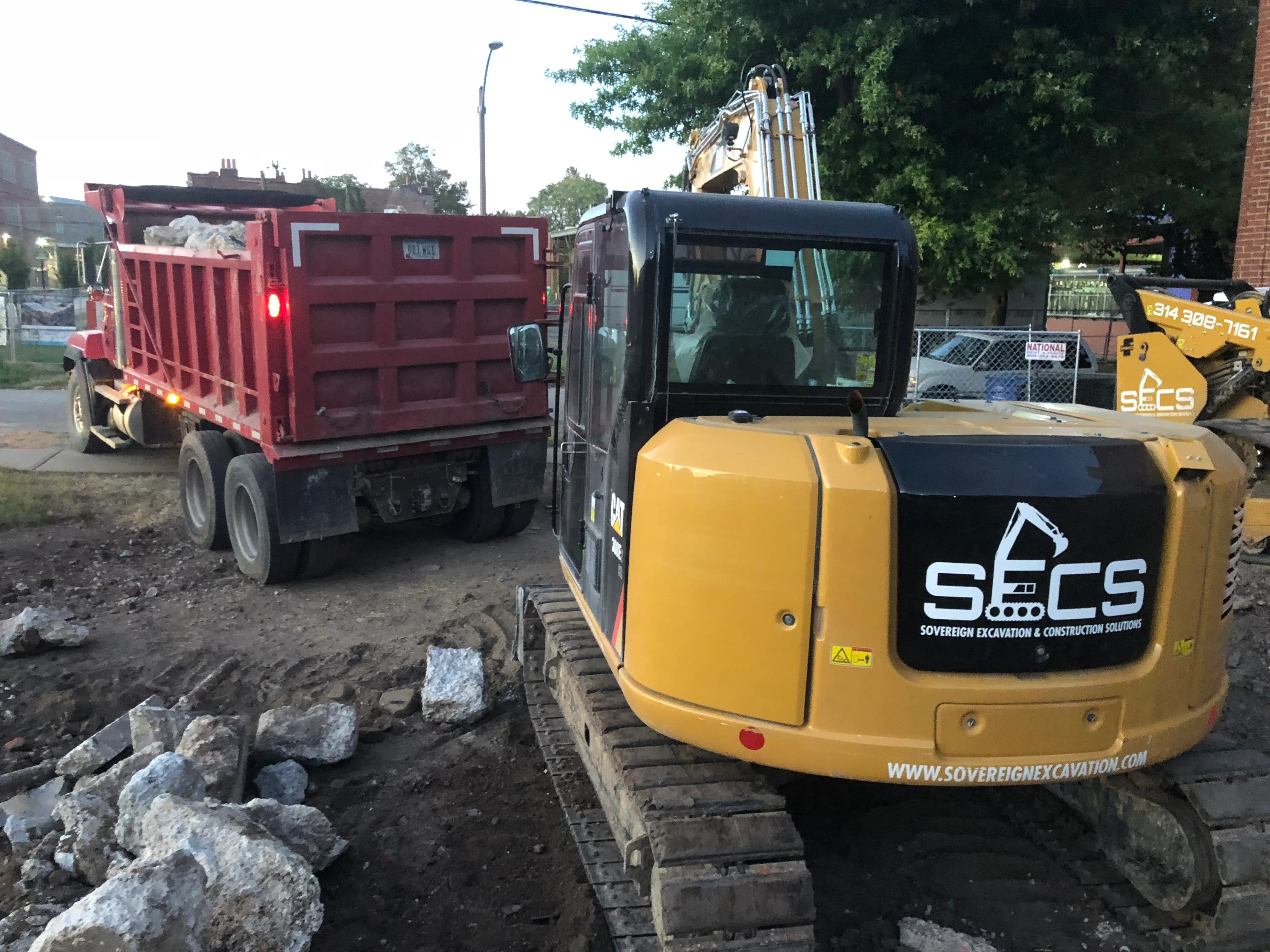 Compact excavator and dump truck removing concrete and masonry debris at demolition site